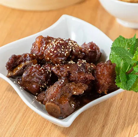 Glazed sesame ribs in a white bowl with fresh mint